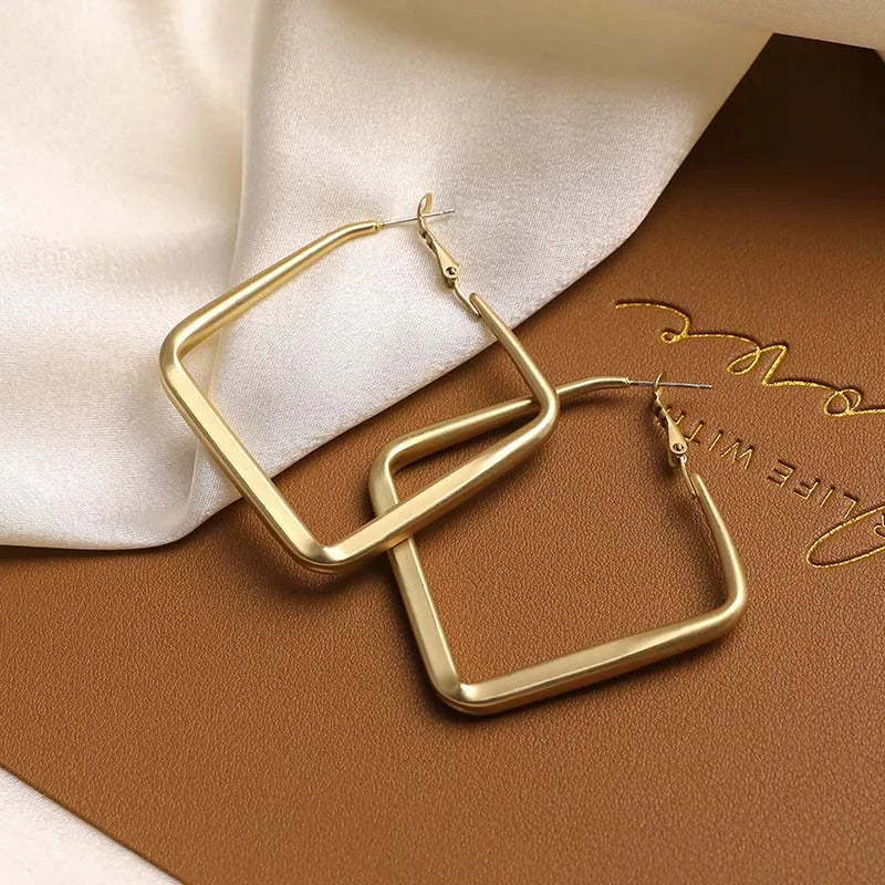 Boucles d’oreilles carrées dorées, paire sur tissu clair, contours épais