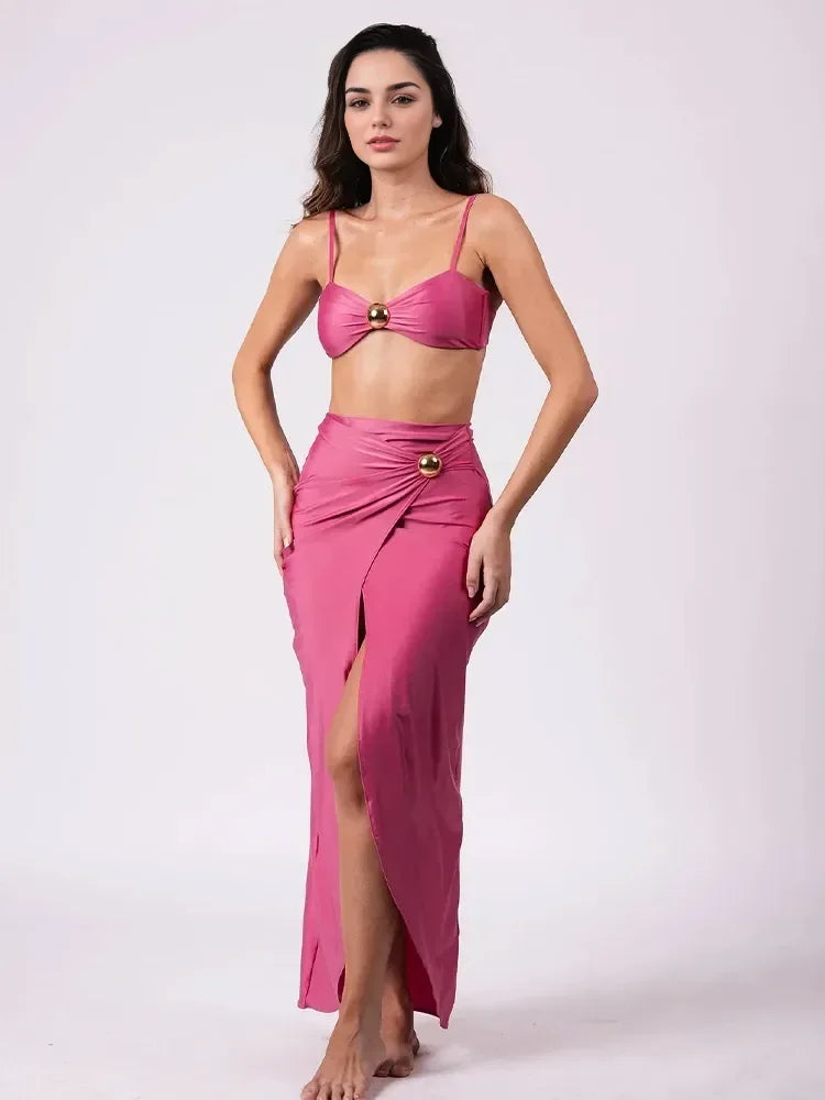 Ensemble maillot 3 pièces rose fuchsia en studio : haut bandeau froncé et jupe longue fendue.