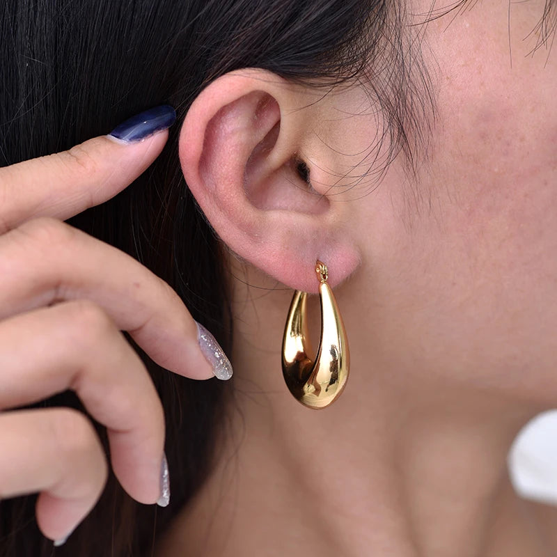 Boucles d’oreilles créoles épaisses dorées portées, vue rapprochée sur l’oreille.