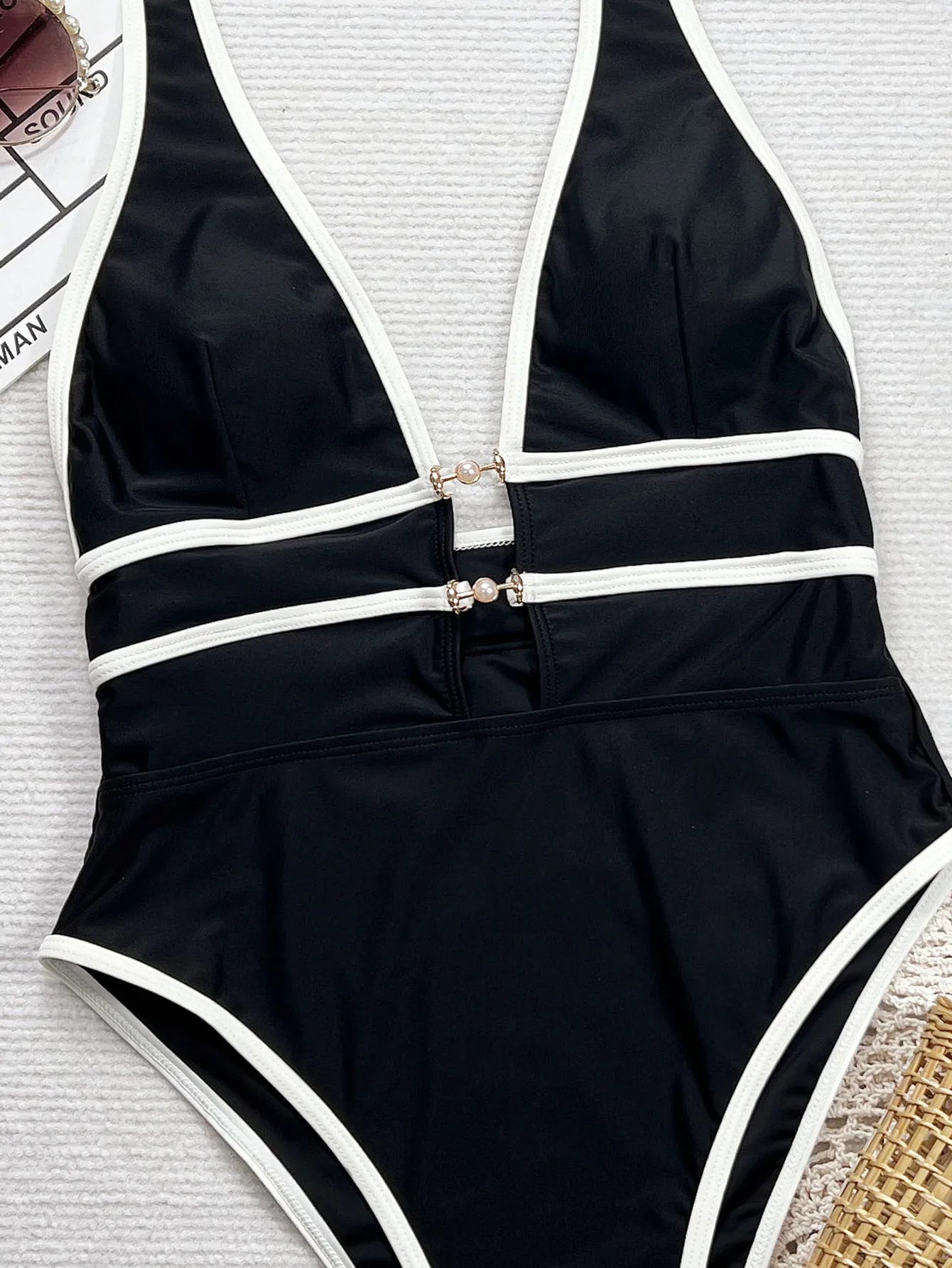 Maillot de bain une pièce noir : gros plan sur buste à bandes blanches et attaches dorées.