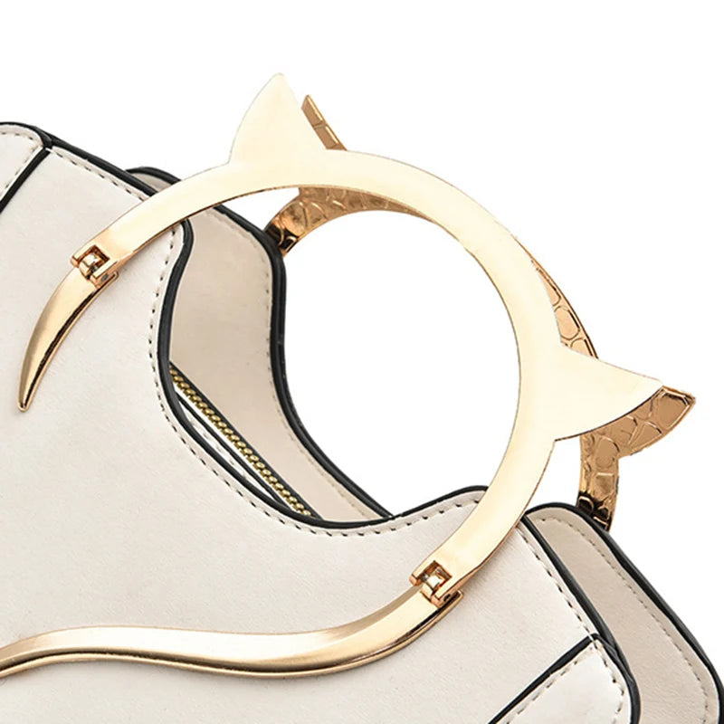 Poignée chat dorée sur mini sac à main blanc cassé, détail du métal et de l’anneau