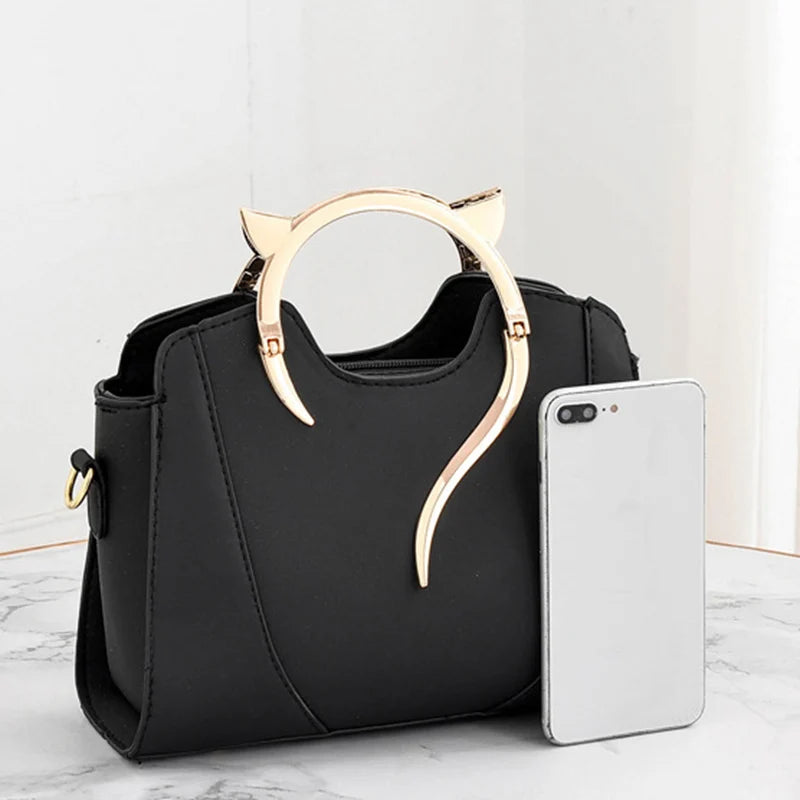 Mini sac à main noir avec poignée chat dorée et bandoulière, gros plan sur l’avant